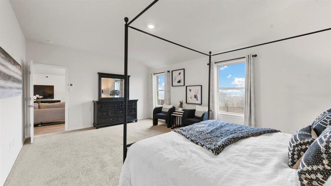 Carpeted bedroom featuring multiple windows with roller shades, recessed lighting, and a doorway opening to a separate living area with wood-finish flooring Carpeted bedroom featuring multiple windows with roller shades, recessed lighting, and a doorway opening to a separate living area with wood-finish flooring