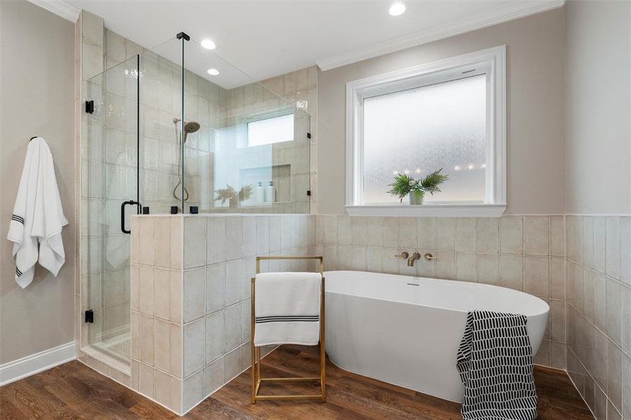 Bathroom featuring tile walls, a shower stall, wood finished floors, ornamental molding, and a soaking tub