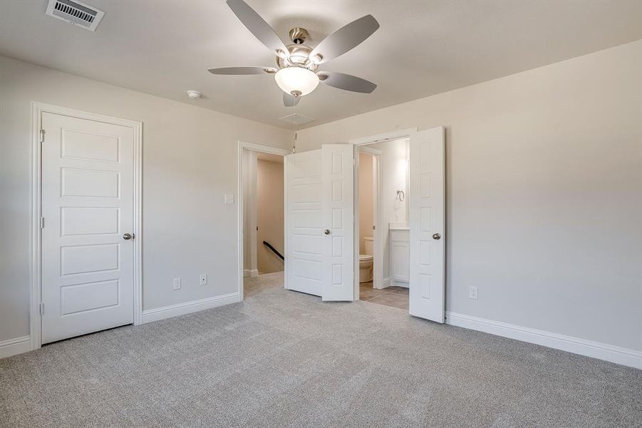 Unfurnished bedroom with light colored carpet, ensuite bathroom, and ceiling fan