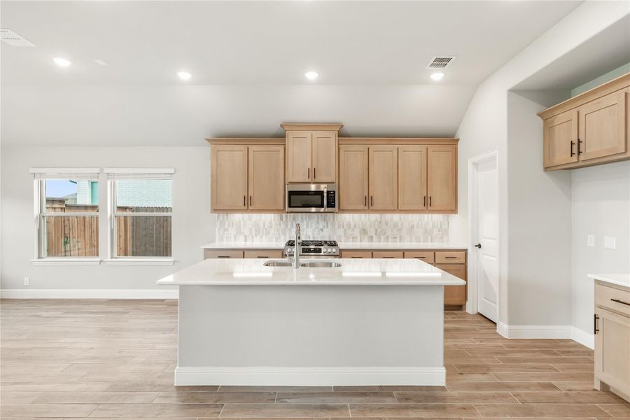 Kitchen with large center island, light wood cabinets, tile backsplash, and stainless steel microwave