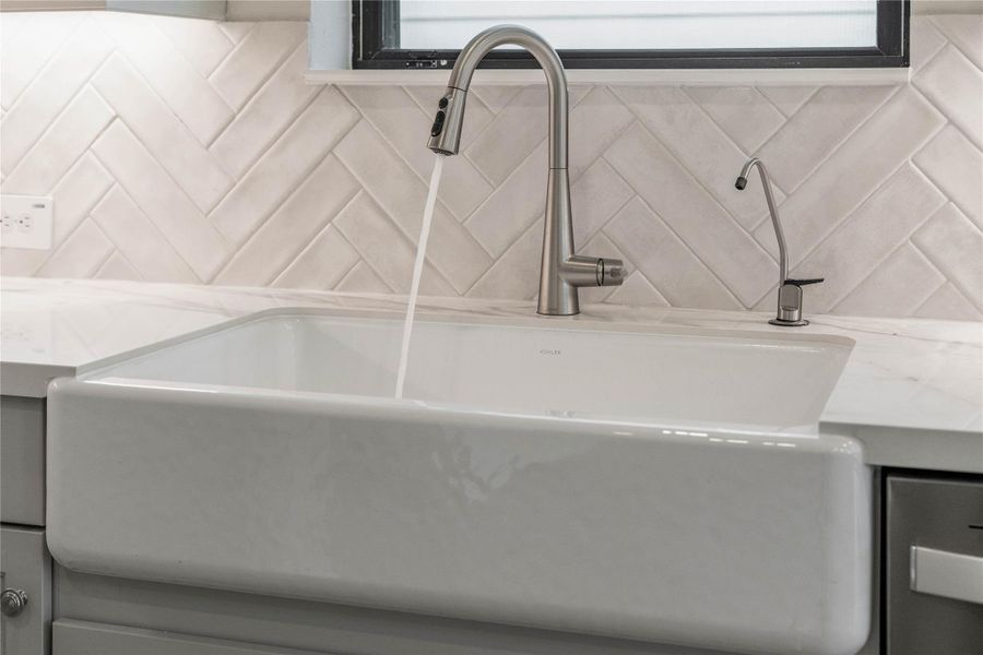 This white porcelain farmhouse sink is complemented by a sleek brushed nickel pull-down faucet and dedicated reverse osmosis tap - all set against a beautiful herringbone tile backsplash and crisp quartz countertops.