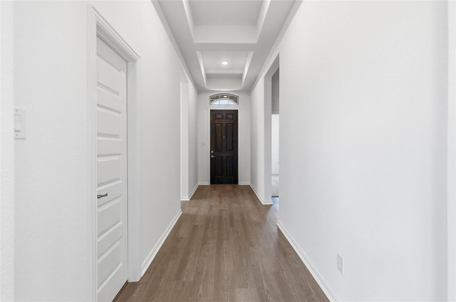 Hallway with wood finished floors and a tray ceiling