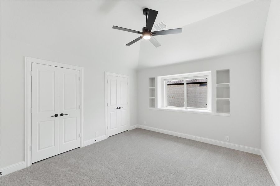 Empty bedroom with vaulted ceiling, ceiling fan, carpet, two closets, and built-in shelves beside window Empty bedroom with vaulted ceiling, ceiling fan, carpet, two closets, and built-in shelves beside window