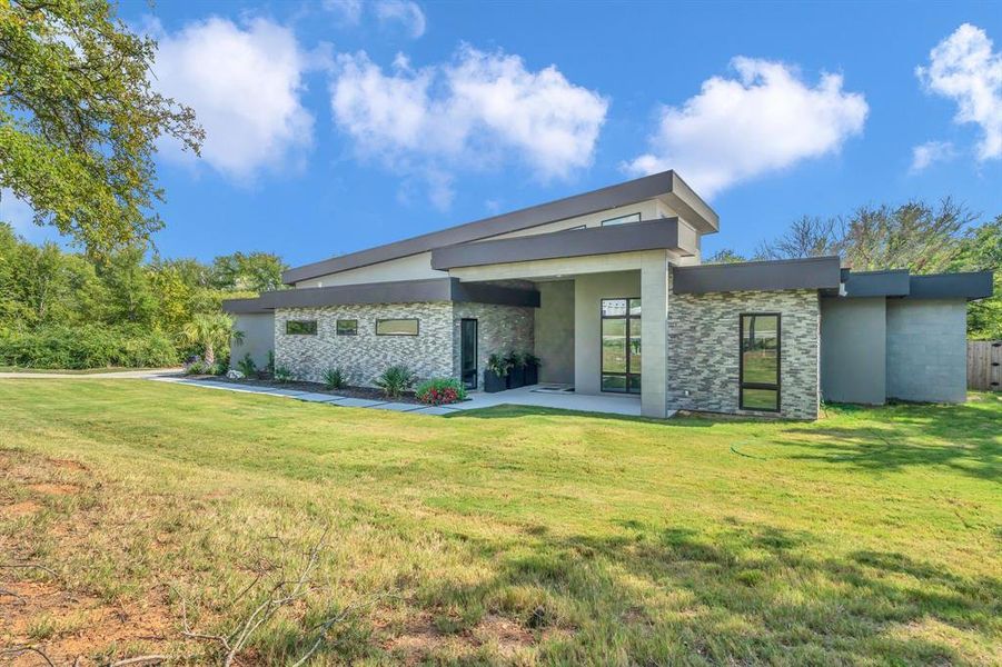 Rear view of house featuring stone siding, a patio area, a lawn, and stucco siding