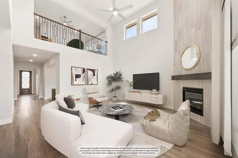 Living room with two-story ceiling, tile fireplace, hardwood floors, and open second-floor balcony overlook