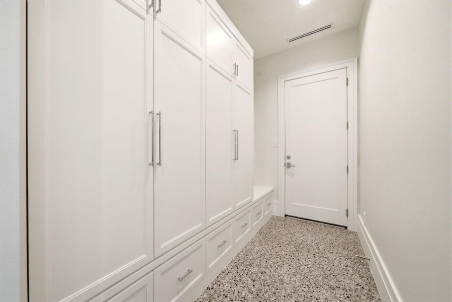 Mudroom-style storage corridor with floor-to-ceiling built-ins, abundant cabinetry, and durable terrazzo-inspired flooring. Mudroom-style storage corridor with floor-to-ceiling built-ins, abundant cabinetry, and durable terrazzo-inspired flooring.