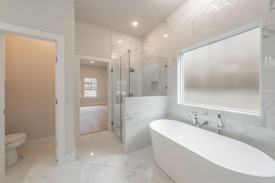 Full bath featuring light marble finish floors, a freestanding tub, a marble finish shower, and recessed lighting