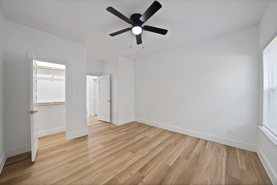 Unfurnished bedroom featuring light wood-style flooring, a spacious closet, and ceiling fan