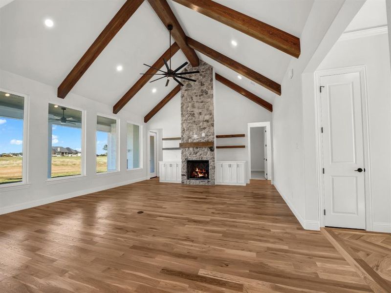 Unfurnished living room featuring a fireplace, beam ceiling, hardwood / wood-style flooring, and high vaulted ceiling