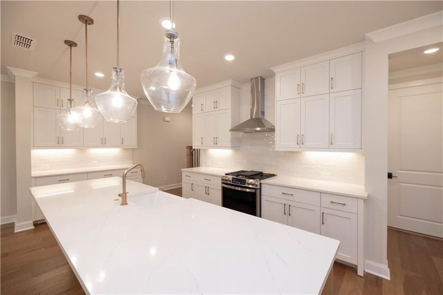 Kitchen with decorative backsplash, decorative light fixtures, wall chimney range hood, stainless steel range with gas cooktop, and white cabinets