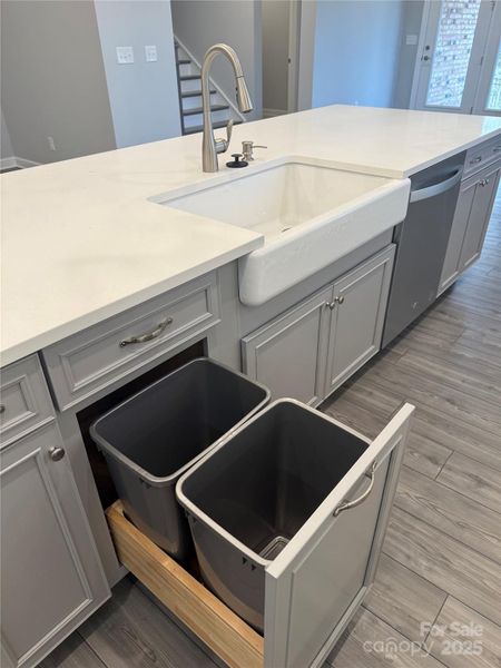 Island features farmhouse sink and roll out garbage cabinet