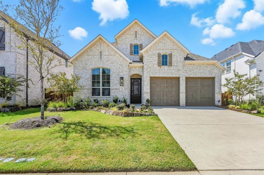 French country style house featuring brick siding, concrete driveway, a garage, and a front yard
