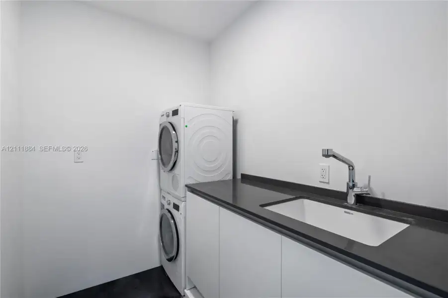 Laundry room featuring white cabinetry, a dark solid-surface countertop, an integrated rectangular basin, and a deck-mounted gooseneck faucet Laundry room featuring white cabinetry, a dark solid-surface countertop, an integrated rectangular basin, and a deck-mounted gooseneck faucet