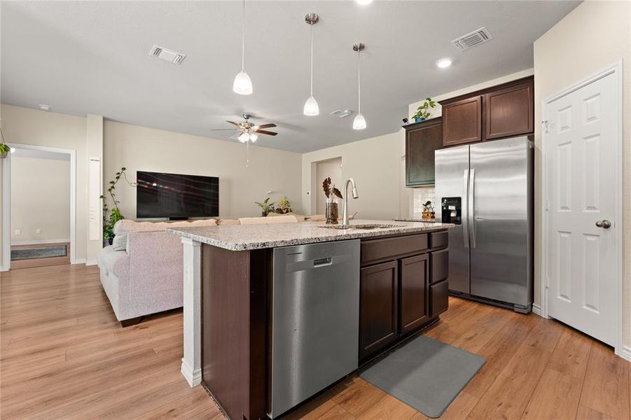 Kitchen with appliances with stainless steel finishes, open floor plan, light stone counters, dark brown cabinets, and light wood-type flooring