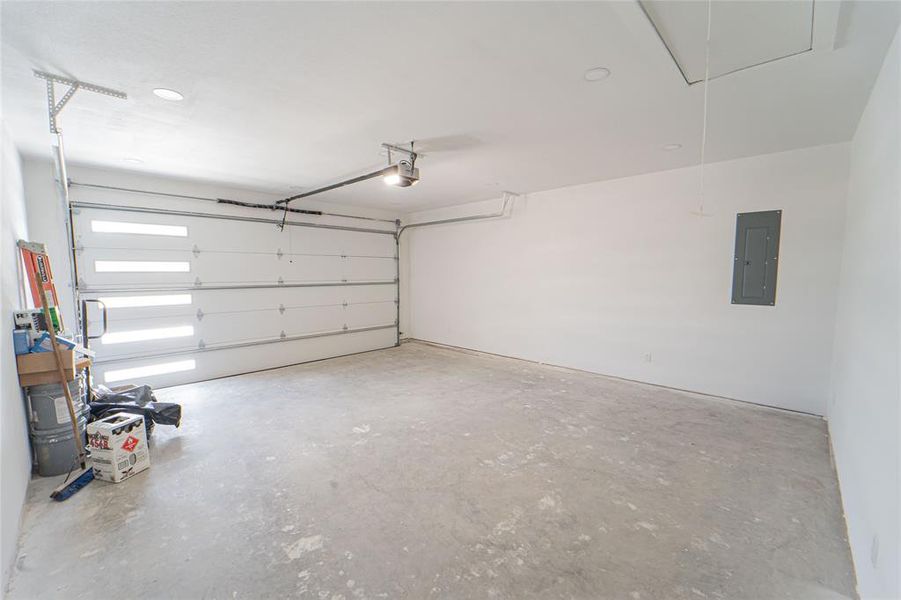 Spacious attached 2 car garage featuring a sectional overhead door with horizontal frosted panels, concrete flooring, overhead lighting, and an automatic garage door opener-offering convenient entry into utility room and kitchen.