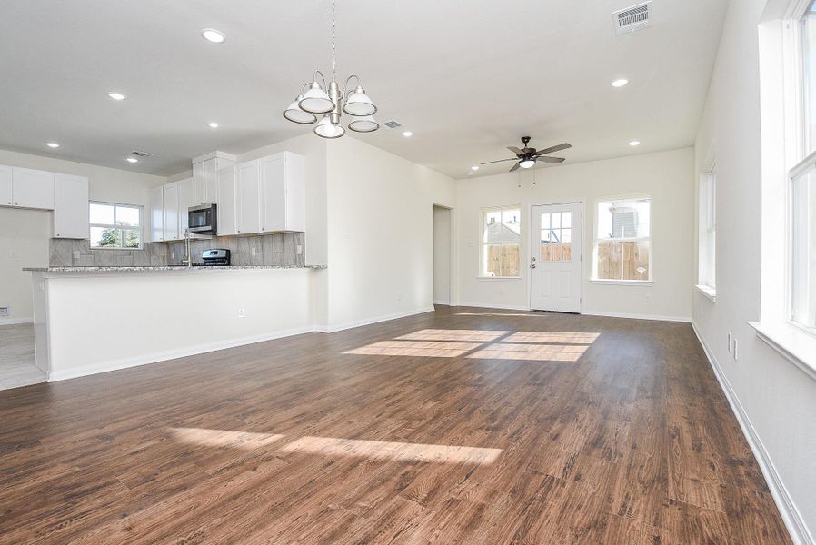 Spacious, empty room with hardwood floors, white kitchen cabinetry, modern appliances, and plenty of natural light from windows and a glass door.