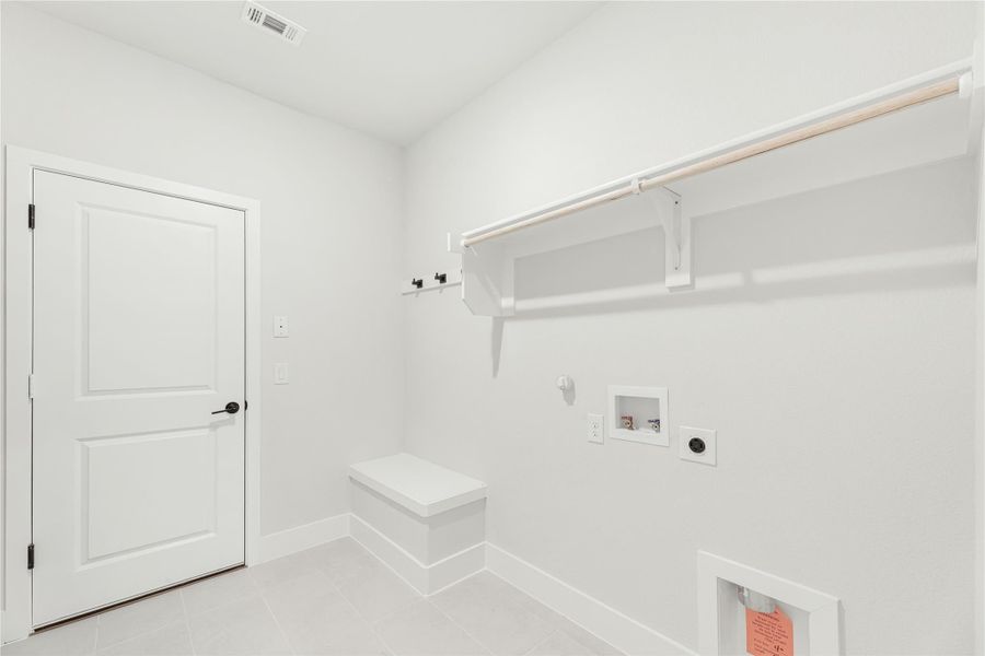 Laundry room with white walls, built-in shelf, hanging rod, bench, and washer and dryer hookups on tile floor
