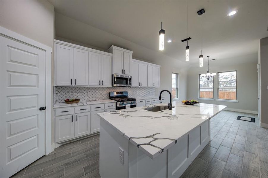 Kitchen featuring decorative light fixtures, white cabinetry, sink, a kitchen island with sink, and stainless steel appliances