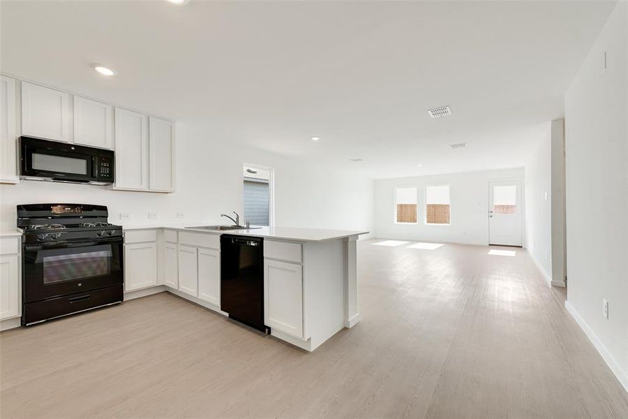 Kitchen with black appliances, white cabinetry, a peninsula, light wood-style floors, and open floor plan