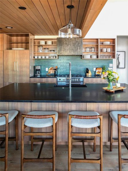 Designer kitchen showcases sleek black countertops, custom wood cabinetry, artisan tile backsplash, and premium appliances.