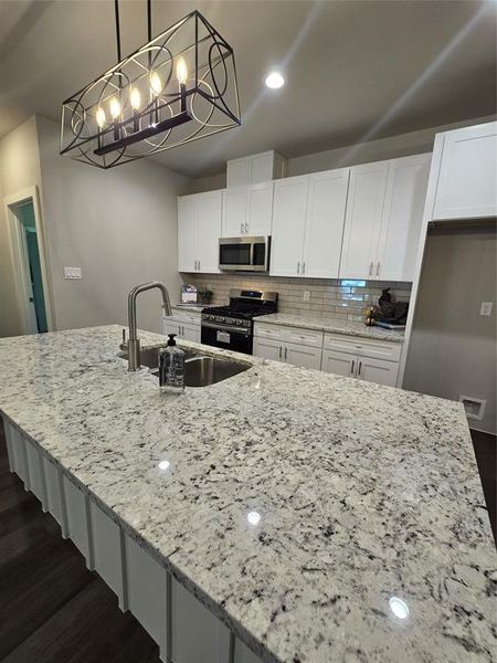 Kitchen with pendant lighting, gas stove, dark wood-type flooring, white cabinetry, and backsplash