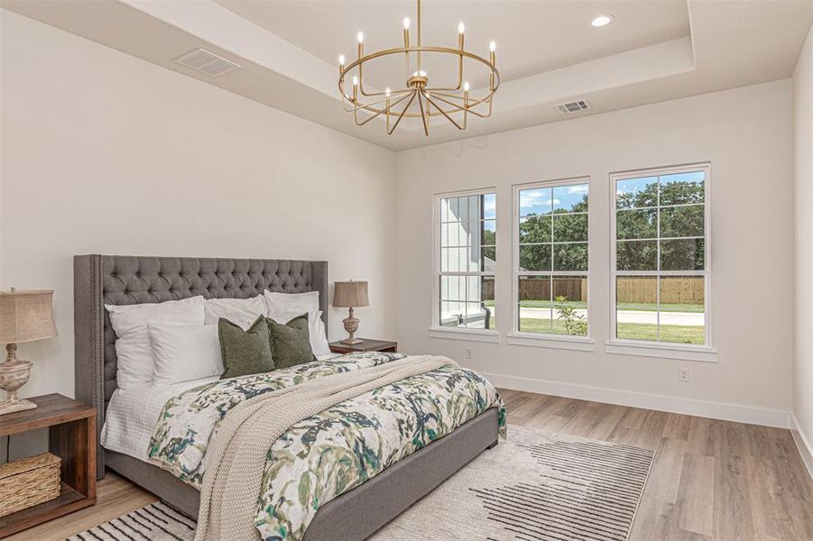 Spacious bedroom featuring light-toned walls, tray ceiling, and recessed lighting
