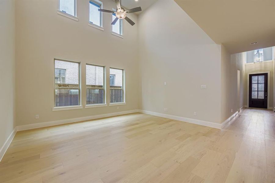 Unfurnished living room featuring light wood-style flooring, a towering ceiling, and ceiling fan Unfurnished living room featuring light wood-style flooring, a towering ceiling, and ceiling fan