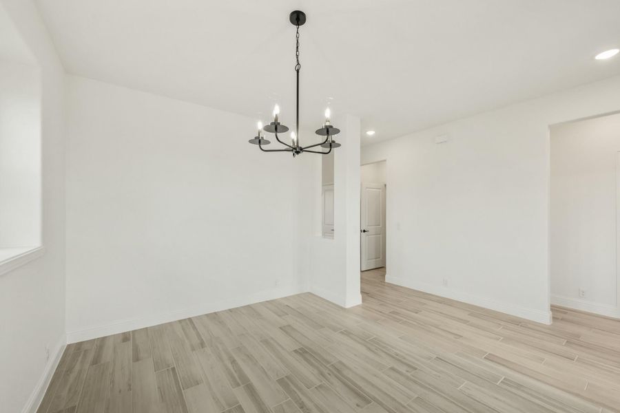 Empty dining room with black chandelier, white walls, and light wood-look tile floors Empty dining room with black chandelier, white walls, and light wood-look tile floors