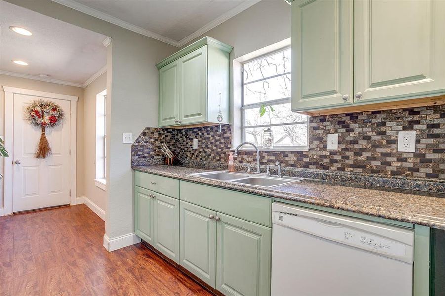 Kitchen with green cabinets, white dishwasher, ornamental molding, light wood-type flooring, and decorative backsplash