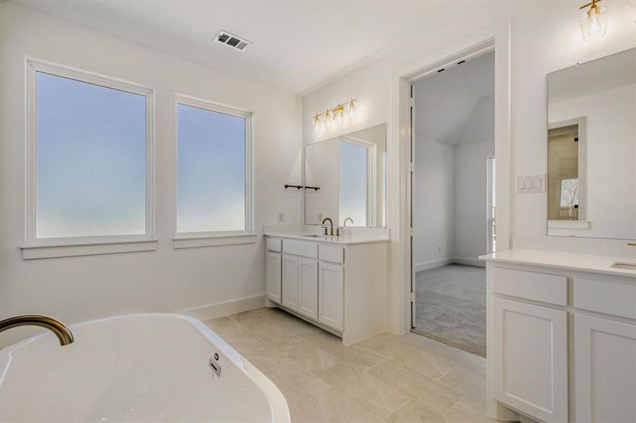 Bathroom featuring two vanities and a soaking tub