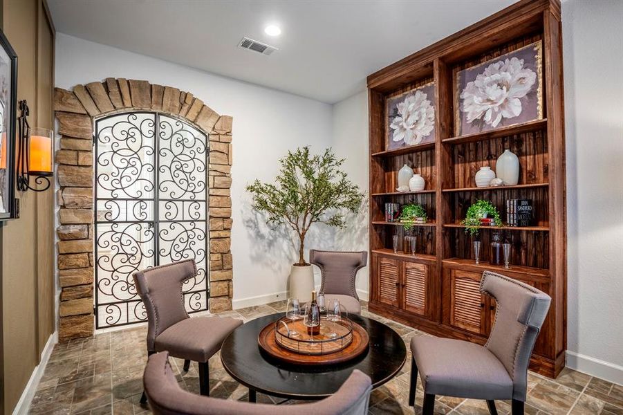 To the right, a large wooden built-in shelving unit displays a mix of decorative items such as vases, framed floral artwork, greenery, and books, contributing to a personalized and sophisticated touch. The flooring is tiled in a natural, stone-like finish, enhancing the earthy and refined atmosphere.