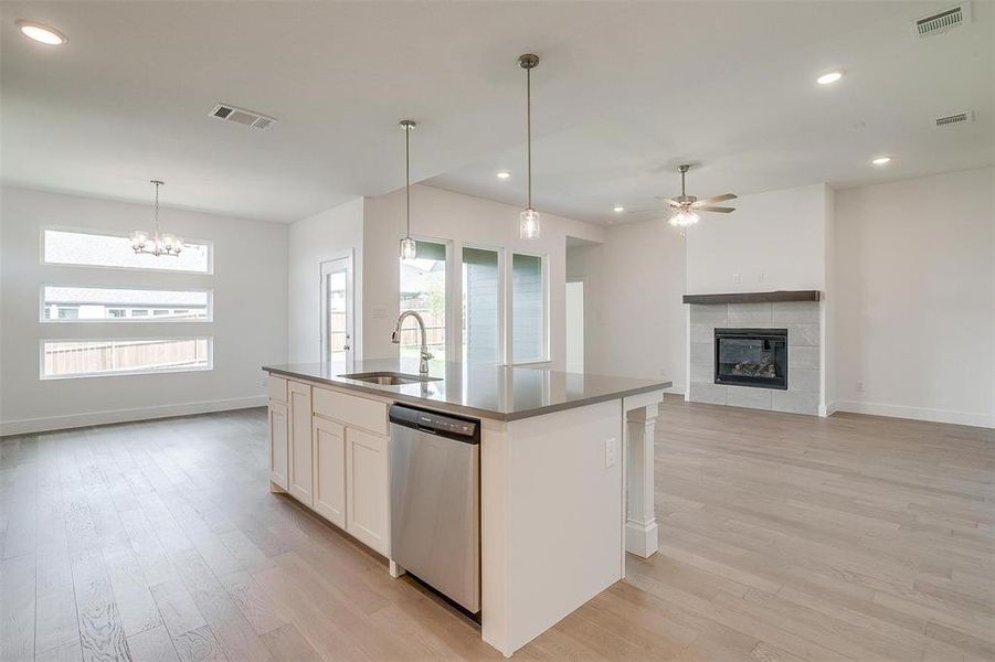 Kitchen with a tiled fireplace, light hardwood / wood-style floors, a kitchen island with sink, and stainless steel dishwasher