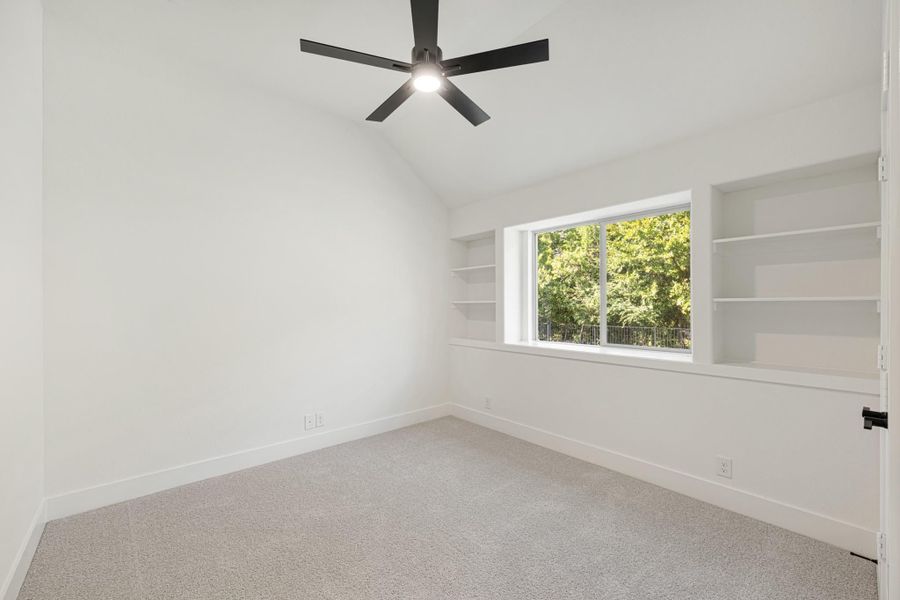 Empty bedroom with vaulted ceiling, black ceiling fan, built-in shelves, and carpet flooring