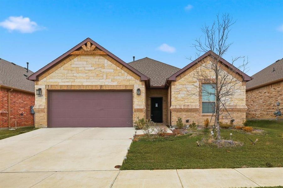 View of front of property featuring stone siding, a front lawn, a garage, driveway, and roof with shingles