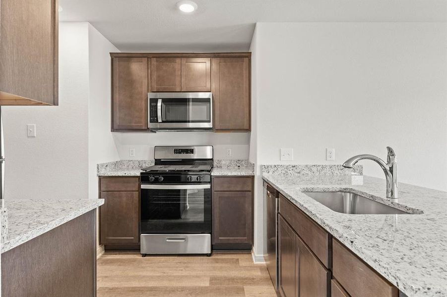 Kitchen featuring light hardwood / wood-style floors, sink, light stone countertops, and stainless steel appliances