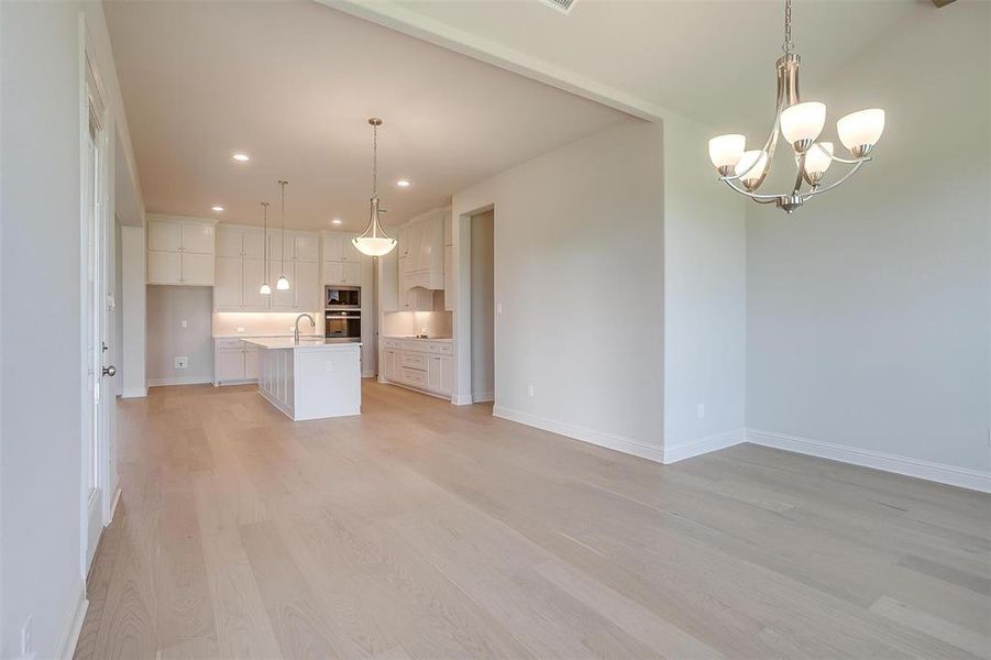 Unfurnished living room featuring sink, a notable chandelier, and light hardwood / wood-style flooring