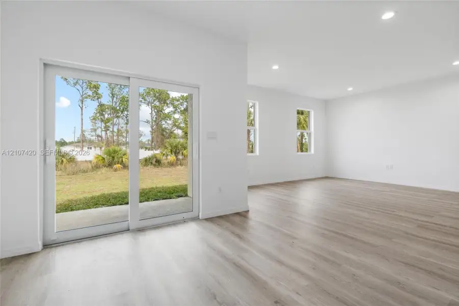 Interior space featuring wood-finish flooring, recessed lighting, and large sliding glass doors leading to an exterior concrete patio Interior space featuring wood-finish flooring, recessed lighting, and large sliding glass doors leading to an exterior concrete patio