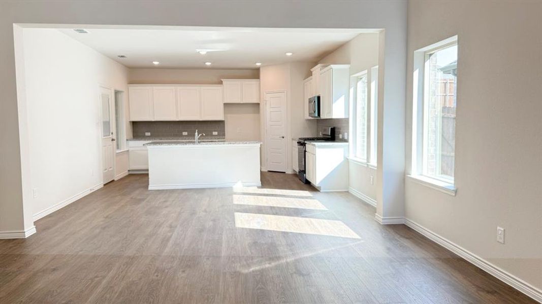Kitchen with white cabinets, decorative backsplash, stainless steel gas range oven, a kitchen island with sink, and dark wood-style floors Kitchen with white cabinets, decorative backsplash, stainless steel gas range oven, a kitchen island with sink, and dark wood-style floors