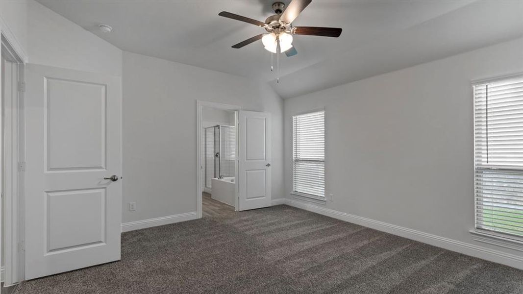 Unfurnished bedroom with ensuite bathroom, vaulted ceiling, ceiling fan, and dark colored carpet
