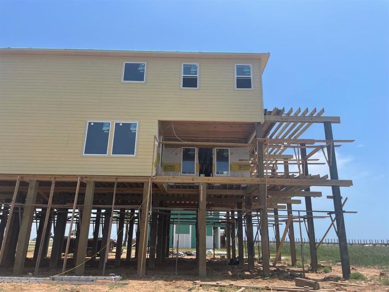 This construction photo shows the east-facing side of the home with visible framing for the screened patio and expansive deck area. The layout maximizes both indoor-outdoor flow and scenic views, with composite decking stretching toward the beach. This construction photo shows the east-facing side of the home with visible framing for the screened patio and expansive deck area. The layout maximizes both indoor-outdoor flow and scenic views, with composite decking stretching toward the beach.