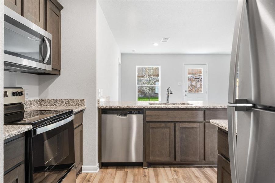 Kitchen with sink, light hardwood / wood-style flooring, appliances with stainless steel finishes, and light stone countertops