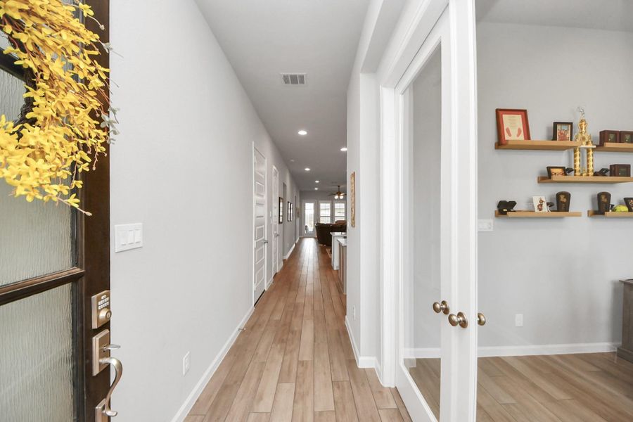 Bright and inviting hallway with wood flooring, recessed lighting, and decorative shelving. Features a glass-paneled door and leads into a spacious home office. Bright and inviting hallway with wood flooring, recessed lighting, and decorative shelving. Features a glass-paneled door and leads into a spacious home office.
