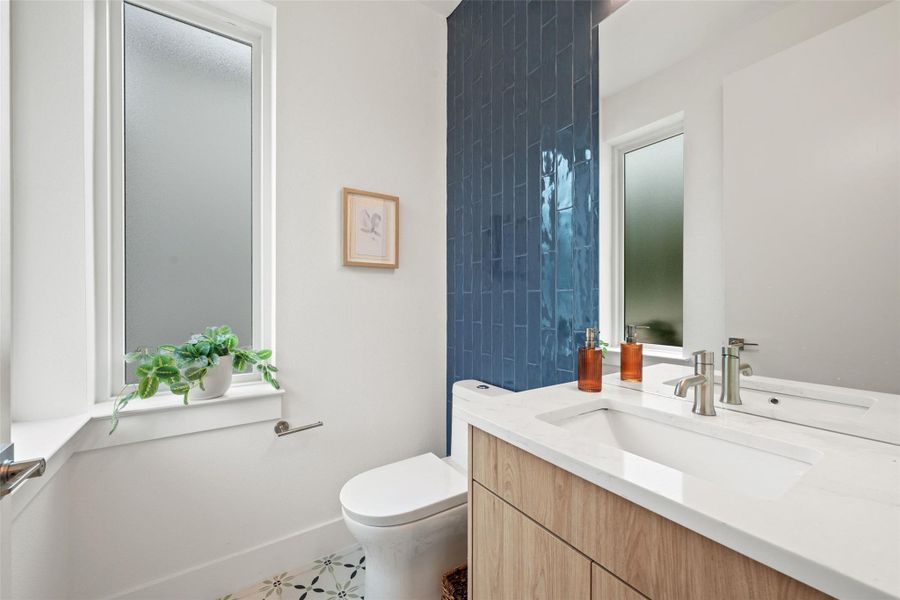 Modern bathroom featuring elegant blue tiled wall, a sleek vanity, and a unique patterned floor. Modern bathroom featuring elegant blue tiled wall, a sleek vanity, and a unique patterned floor.