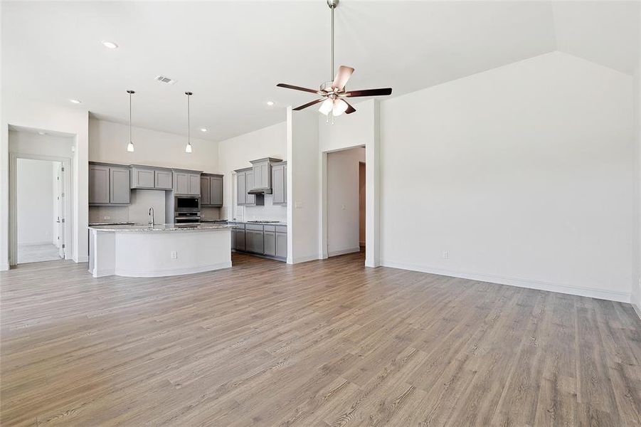 Unfurnished living room featuring ceiling fan, light wood-style floors, and vaulted ceiling