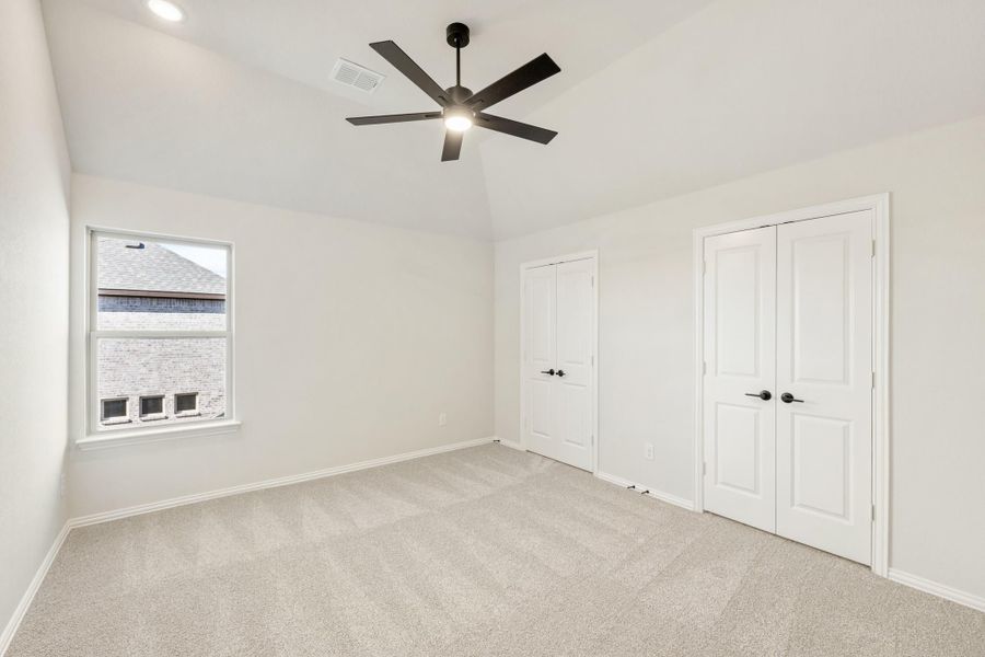 Empty bedroom with vaulted ceiling, black ceiling fan, carpet flooring, and double doors
