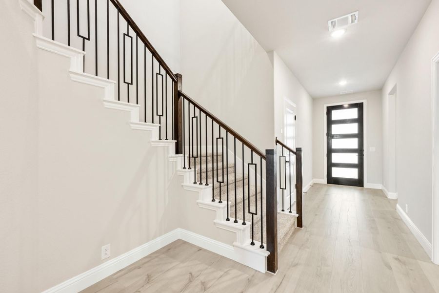 Entryway with carpeted staircase, black iron balusters, wood handrail, and glass front door with light wood floors