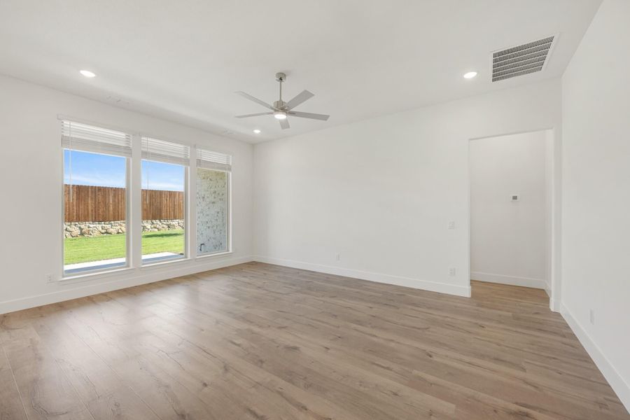 Empty room with hardwood floors, ceiling fan, and large windows overlooking a backyard Empty room with hardwood floors, ceiling fan, and large windows overlooking a backyard