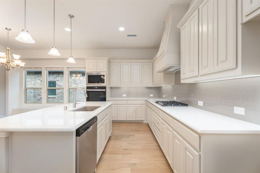 Kitchen featuring tasteful backsplash, hanging light fixtures, light wood finished floors, stainless steel appliances, and an island with sink