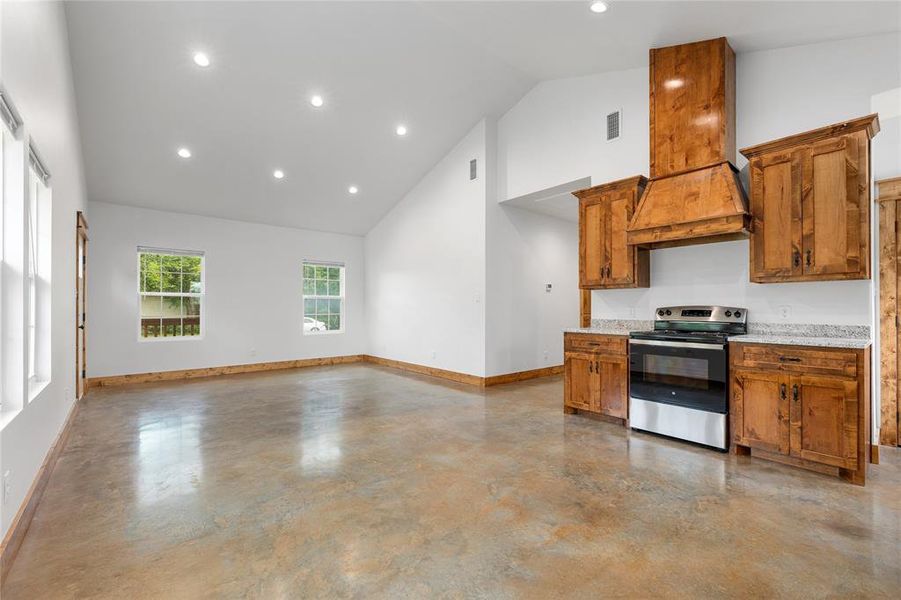 Kitchen featuring electric stove, high vaulted ceiling, baseboards, concrete flooring, and brown cabinetry Kitchen featuring electric stove, high vaulted ceiling, baseboards, concrete flooring, and brown cabinetry
