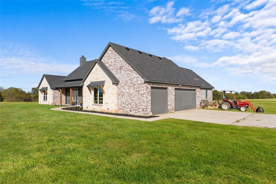 Brick and stone exterior featuring a dark asphalt shingle roof, attached two-car garage with gray doors, covered entry porch with wood columns, and a concrete driveway